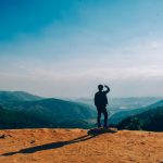 pexels-photo-1087735-1087735 A lone traveler stands on a hilltop, gazing over a vast mountain landscape under a clear blue sky.